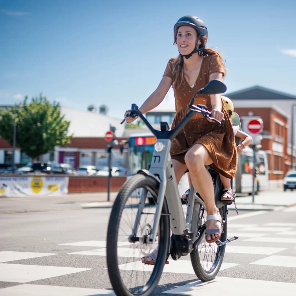 Fietser met kindje achterop steekt zonnig kruispunt over